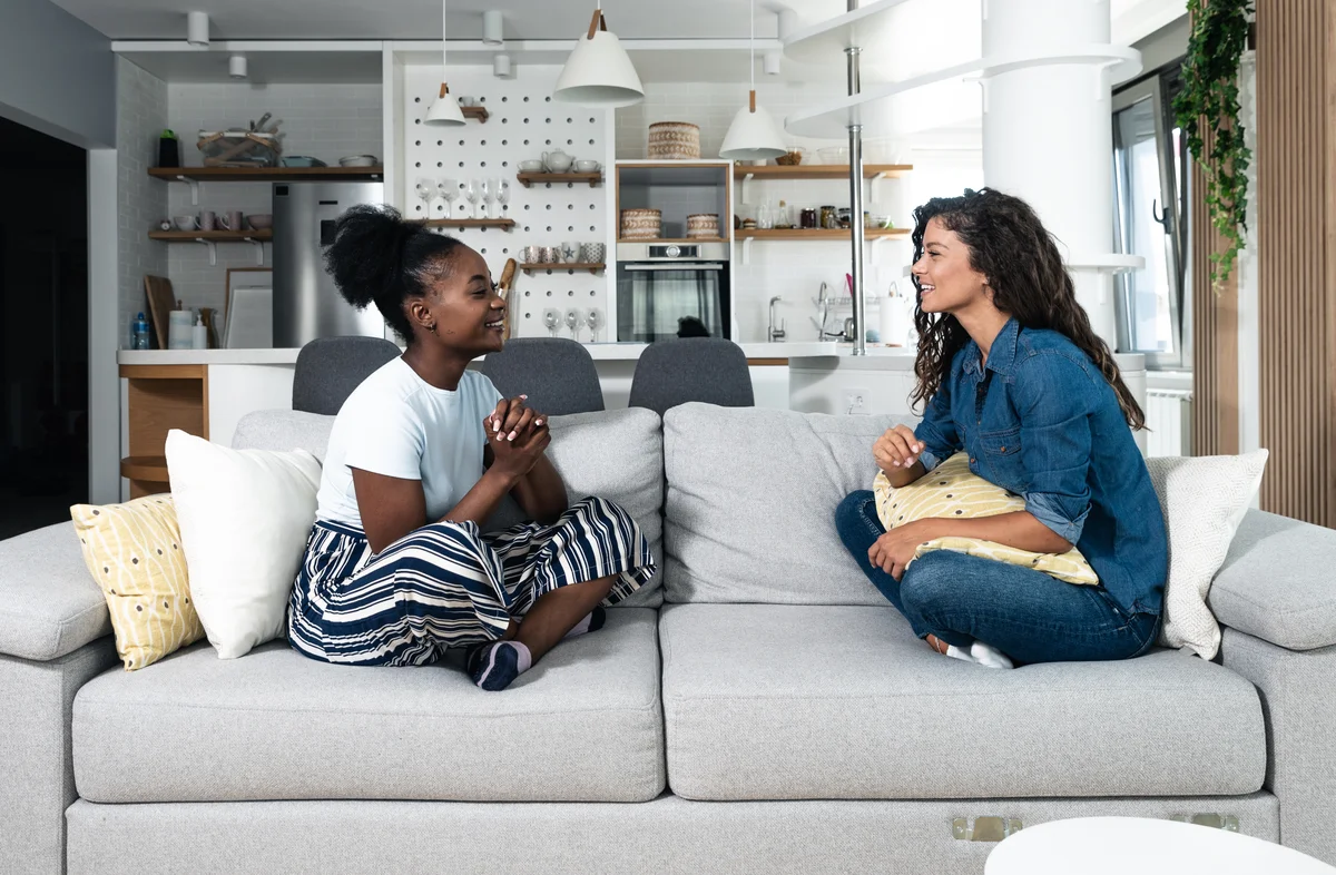 Two women sit on a sofa and face each other.