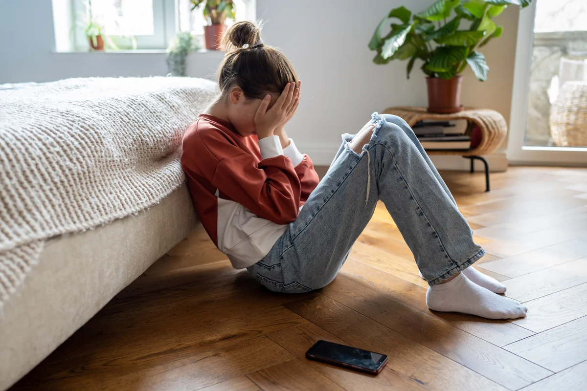 A teen sits on the floor and holds her head in her hands.
