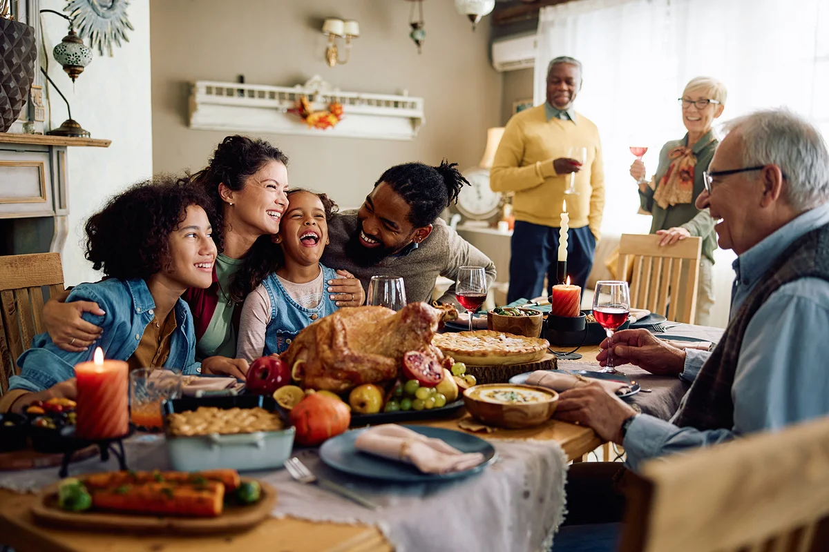 Happy multiracial parents and their kids laughing during family meal on Thanksgiving in dining room