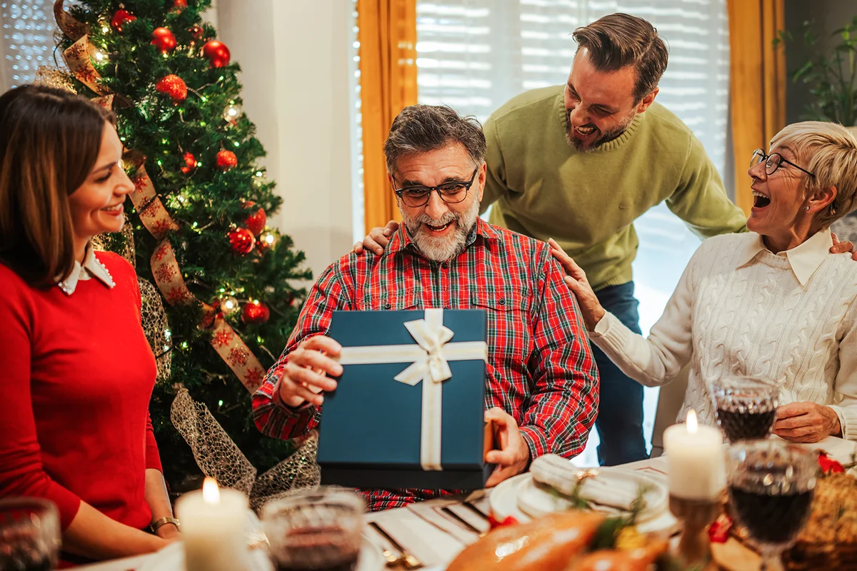 Family is gathered around a festive table enjoying their christmas dinner and giving a present