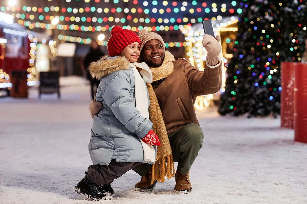 father and daughter taking selfie photo outdoors together in Christmas market