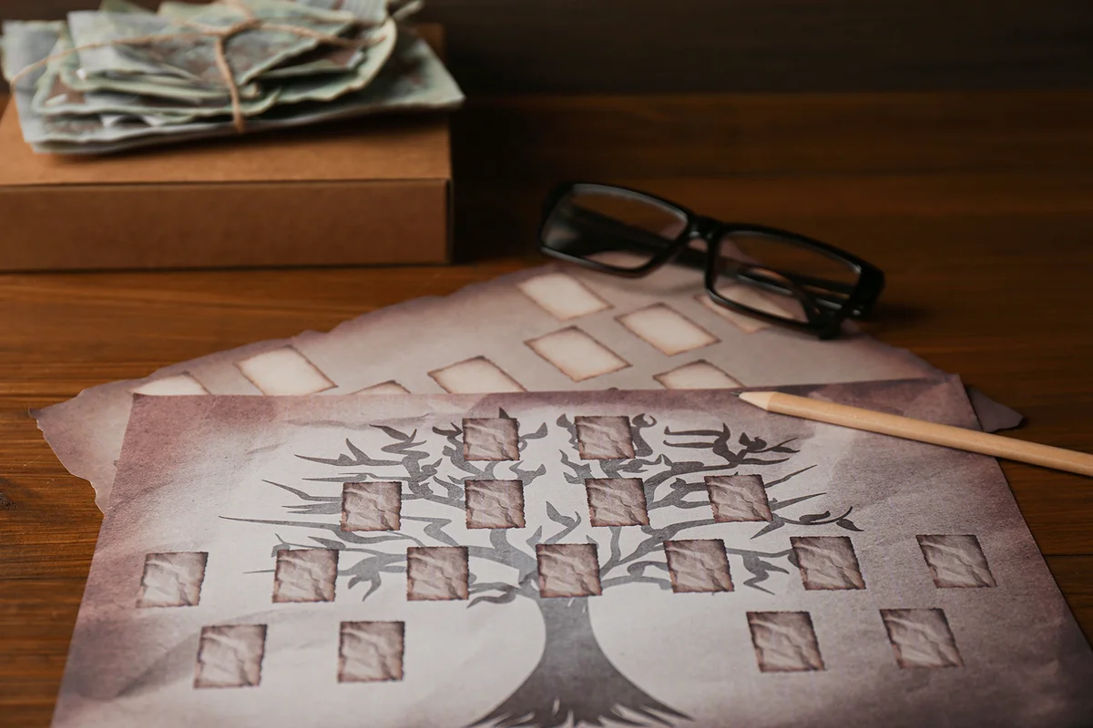 Papers with family tree templates, pencil, photos and glasses on wooden table