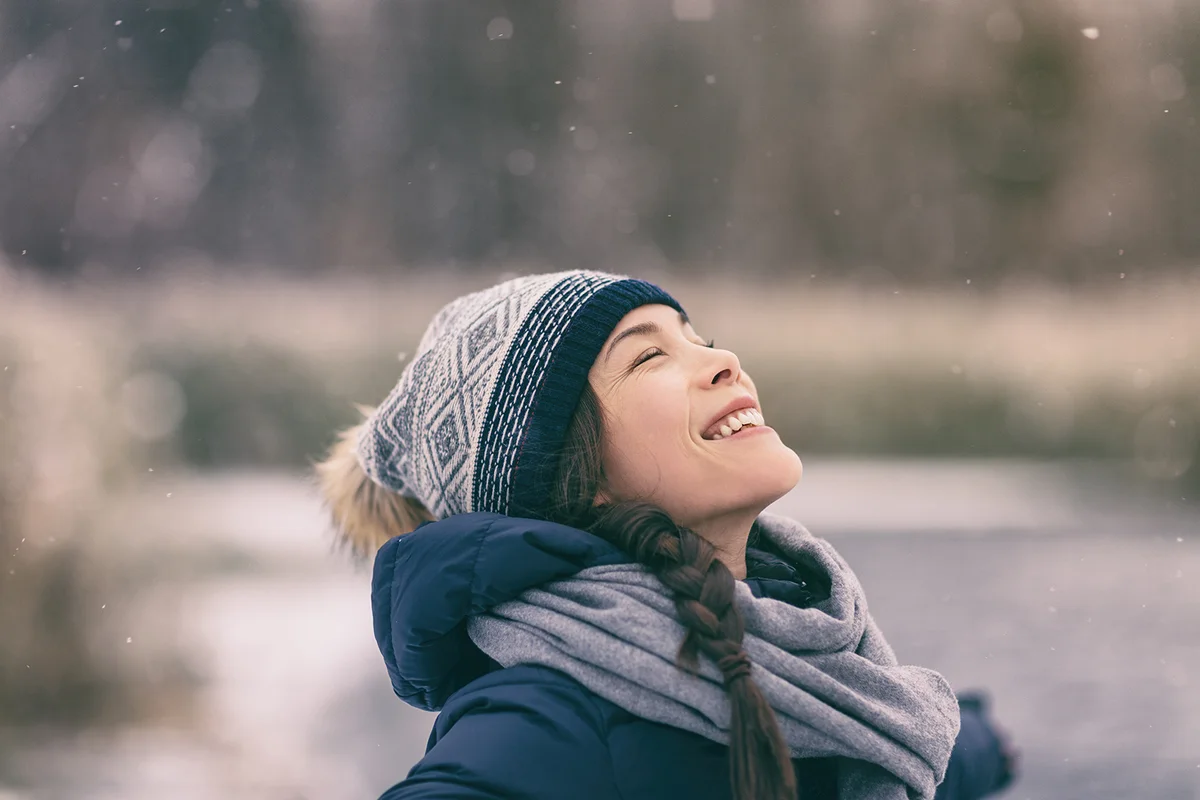 Winter woman happy enjoying snow falling on face outdoor forest nature