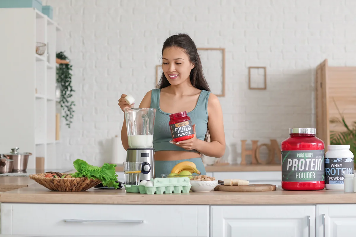 Sporty young happy Asian woman making protein shake at home
