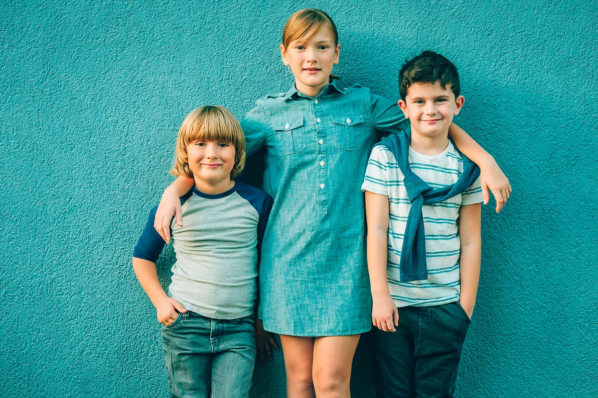 Outdoor portrait of 3 fashion kids posing against blue background