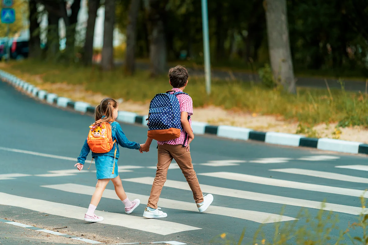 girl and boy with backpacks carefully cross road on pedestrian crossing on their way to school. Traffic rules. Walking path along zebra in city. concept of pedestrians crossing pedestrian crossing.