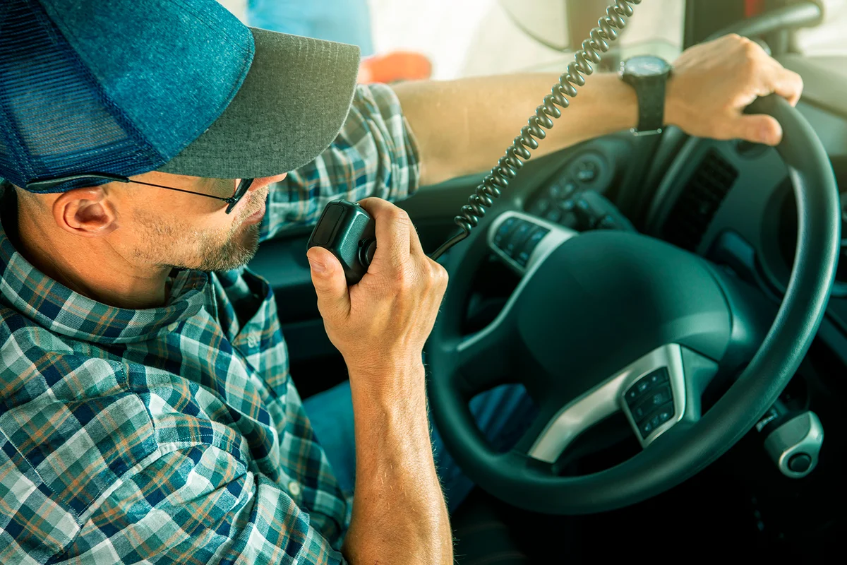 Caucasian Trucker in His 40s Making Conversation Using CB Radio Inside His Semi Truck Cabin. Convoy Truck Drivers Communication Theme.