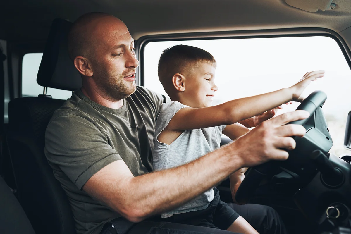 Father teaches little son to drive on road trip