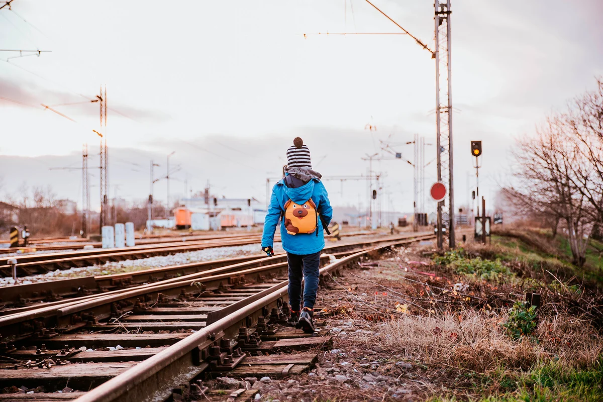 A little boy with a backpack on his back is walking on the railroad tracks
