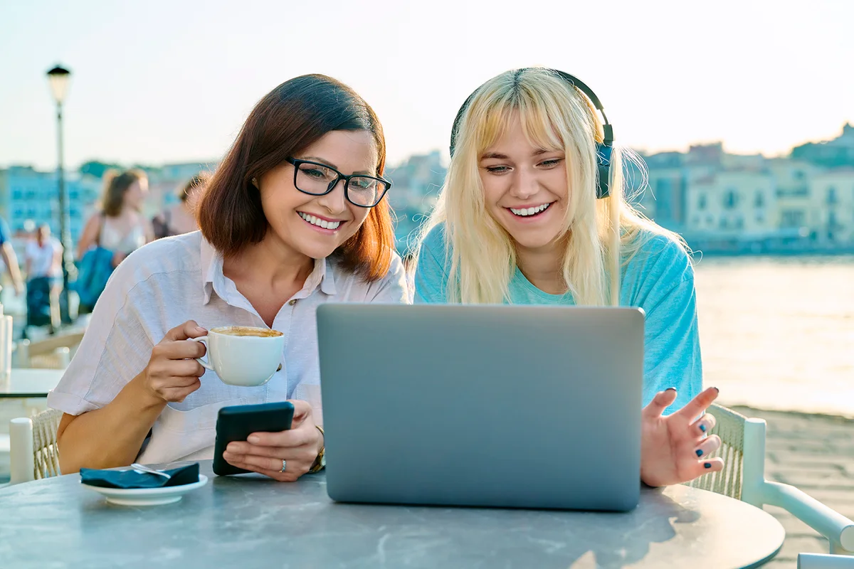 Mom and teenage daughter looking at laptop together, sitting in an outdoor cafe