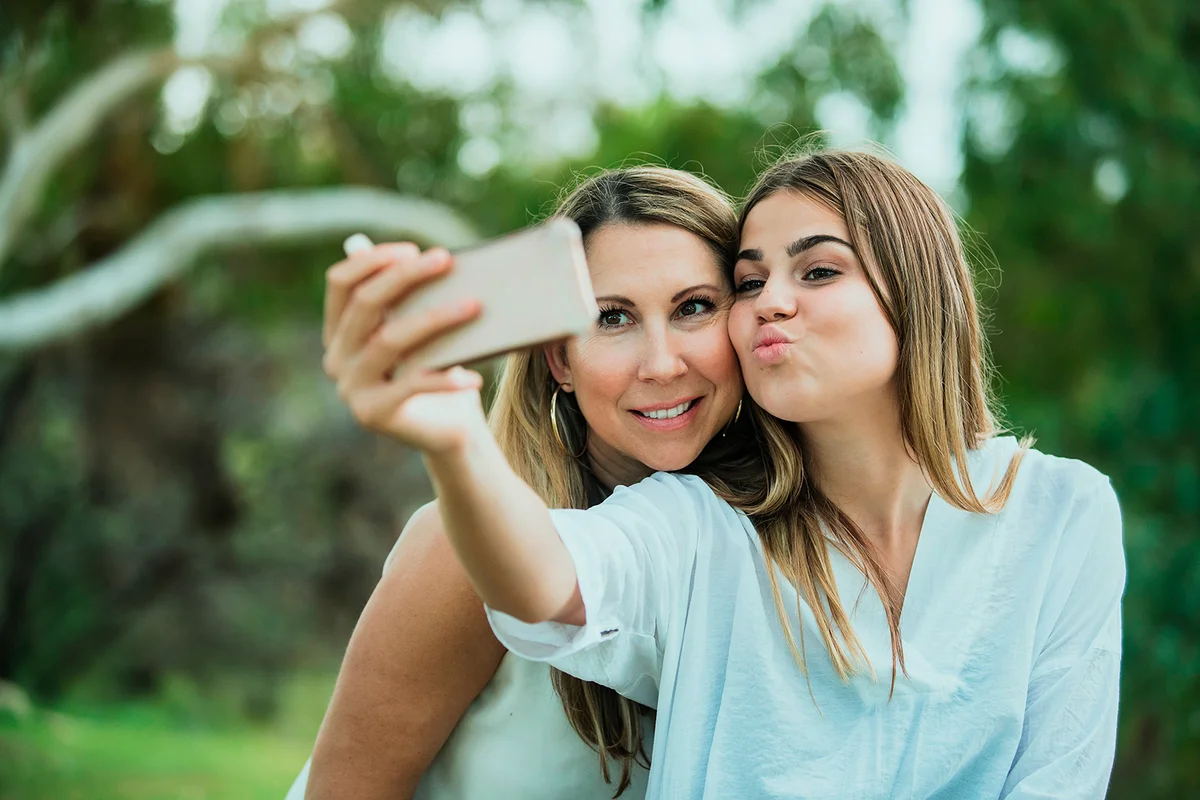 A mother and daughter are side by side in the park posing for a selfie
