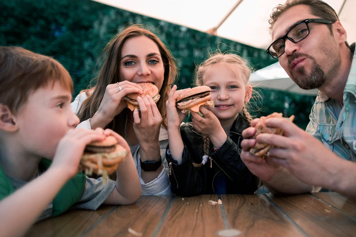 happy family eating burgers sitting at a table in a cafe