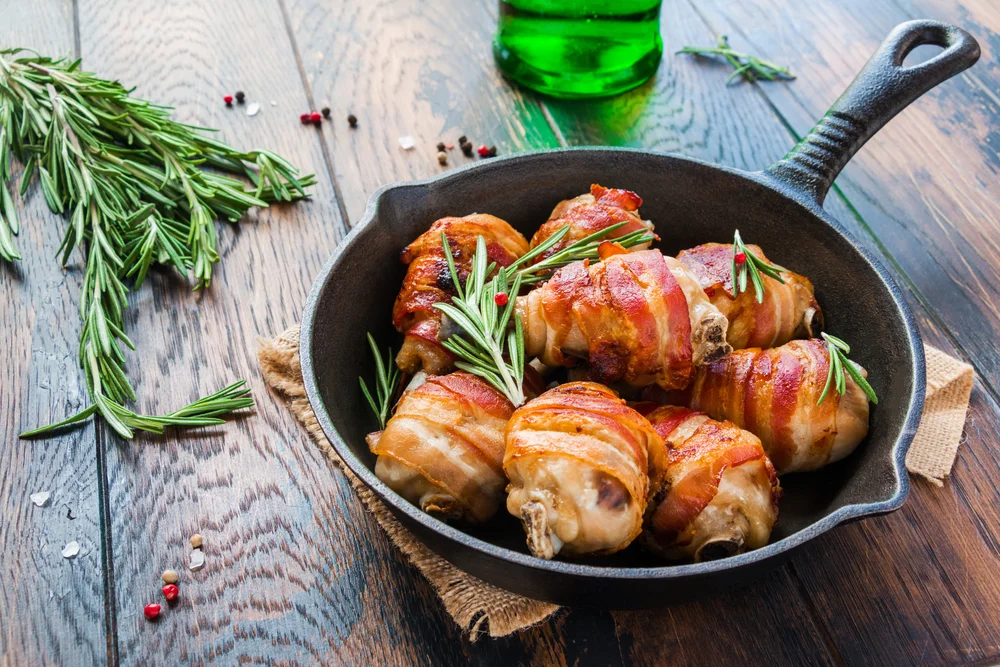 Bacon wrapped chicken drumsticks in a black cast-iron