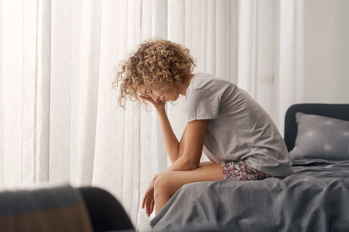 Tired unhappy woman waking up and sitting on her bed