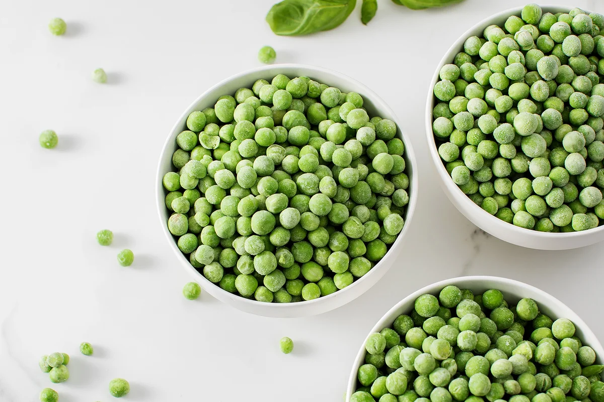 Three bowls of frozen green peas on a marble surface