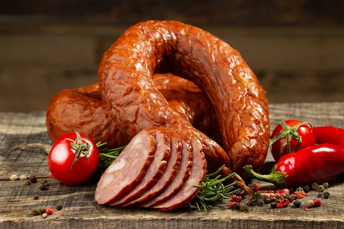 Sliced kielbasa with vegetables on wooden background