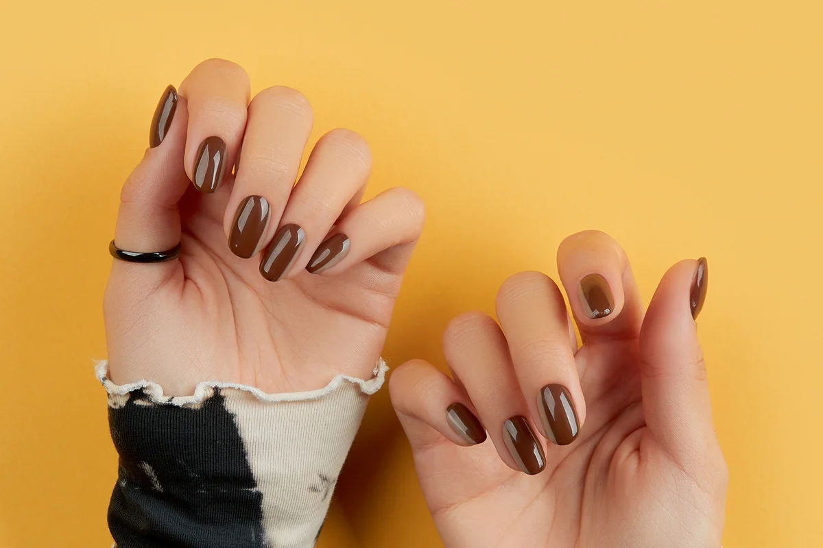 womans hands with brown nail design on yellow background