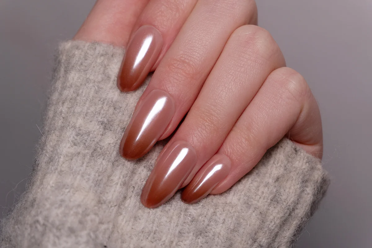woman’s hand in a gray sweater with manicure in soft pink-to-brown tone