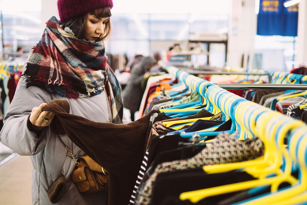 Young woman is browsing a rail of clothes at mall store