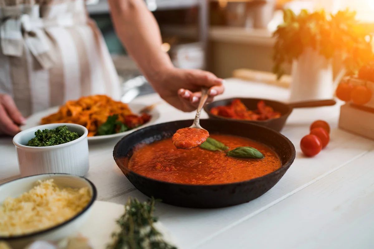 Woman making homemade pasta with tomato sous and cheese over old wooden table