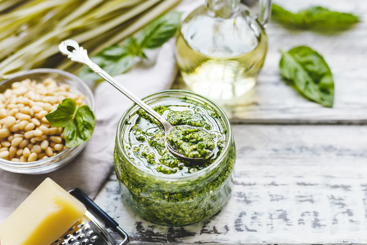 glass jar of pesto sauce with ingredients on rustic white wooden table