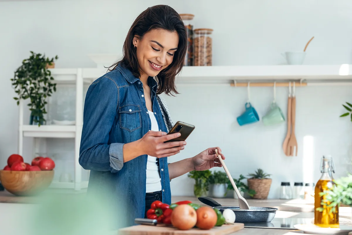 woman using her mobile phone while cooking vegetables in the kitchen at home