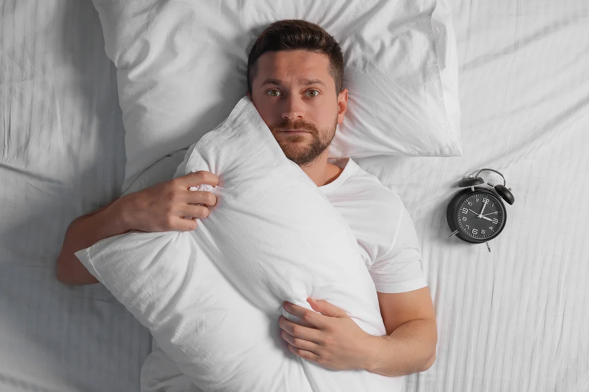 Sleepy man with pillow and alarm clock in bed