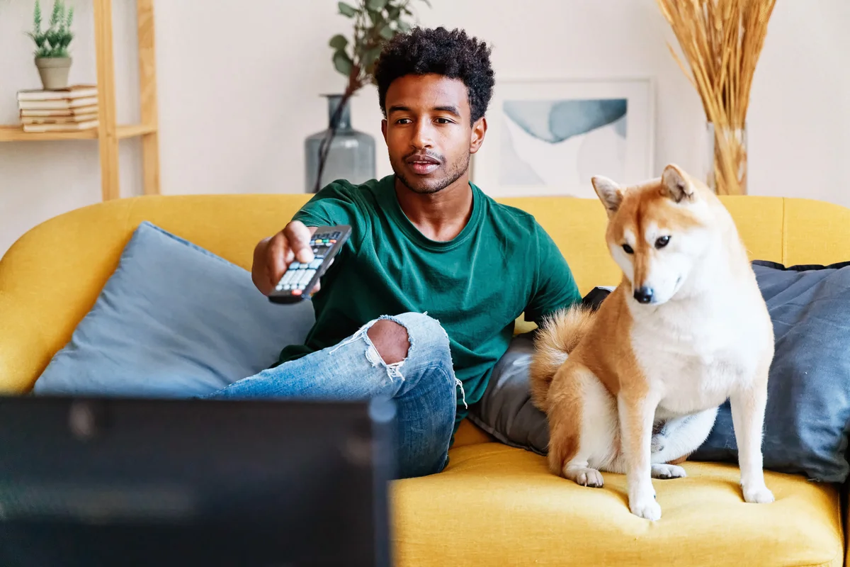 Man sitting on sofa in living room with dog watching TV