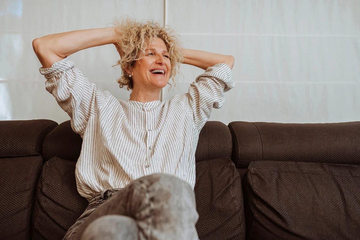 Happy beautiful relaxed middle aged woman drinking coffee relaxing on sofa at home