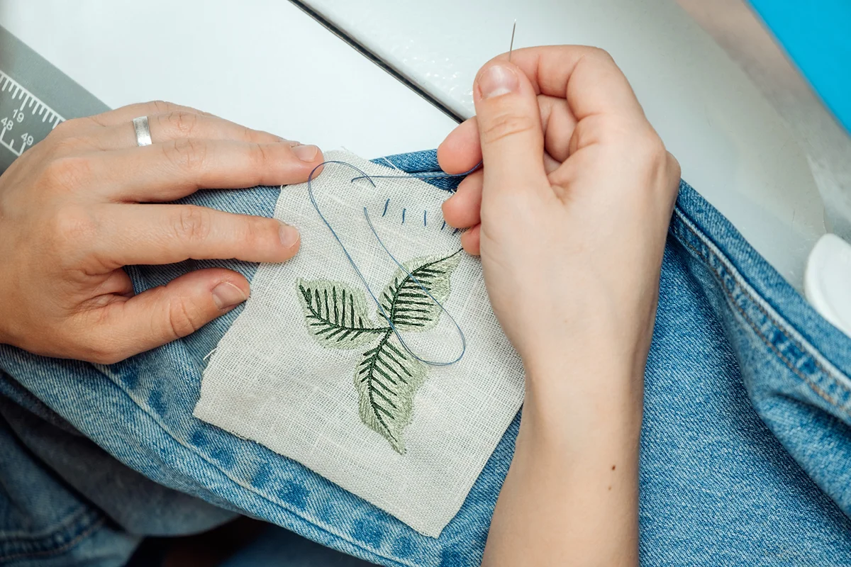 A woman mends jeans, sews a patch on a hole