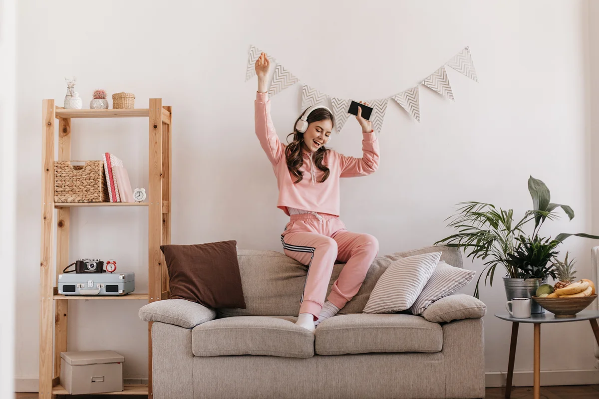 Charming girl in tracksuit dancing, sitting on couch