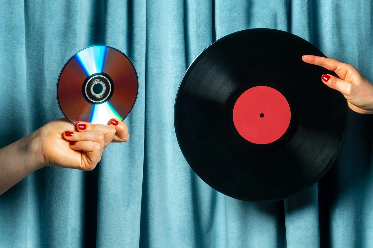 Female hand holding vinyl record and cd disc against blue velvet curtain
