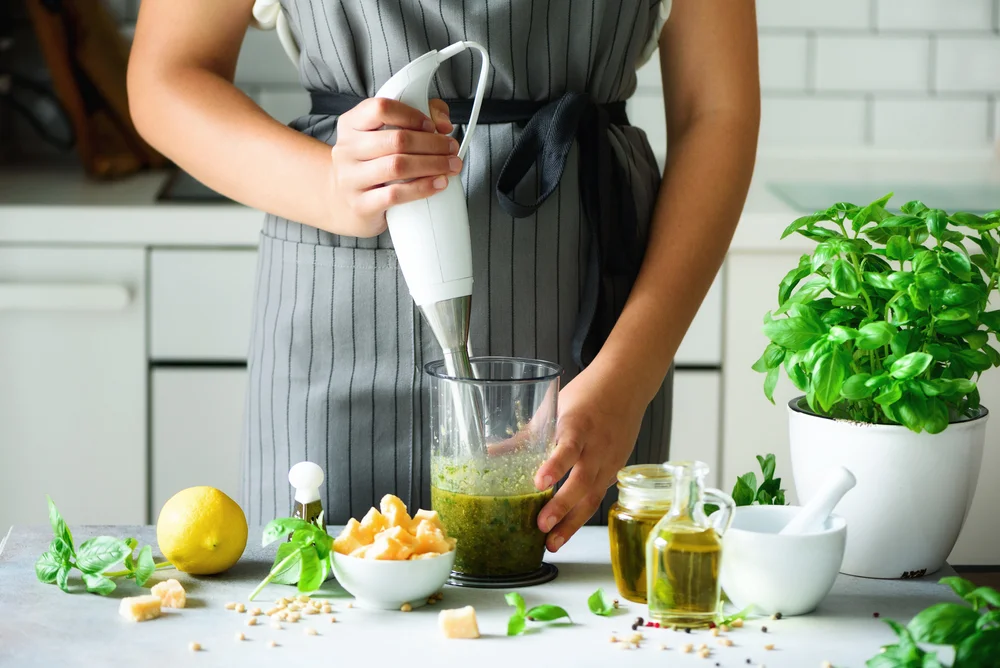 closeup of a woman making pesto with an immersion blender
