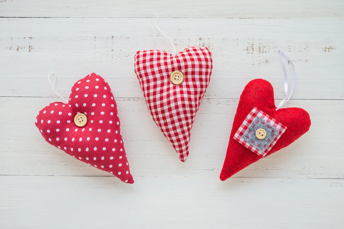 Three red handmade sewed hearts on white wooden background