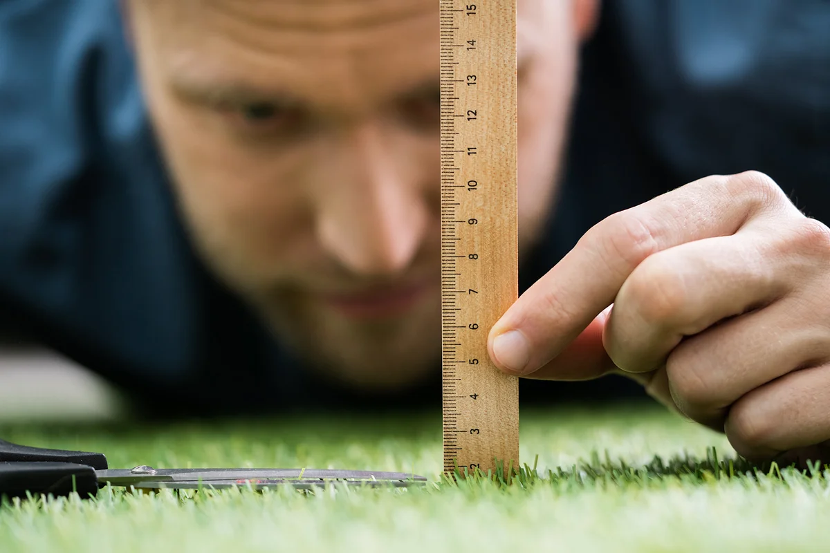 Close-up Of A Man Cutting Green Grass Measured With Ruler