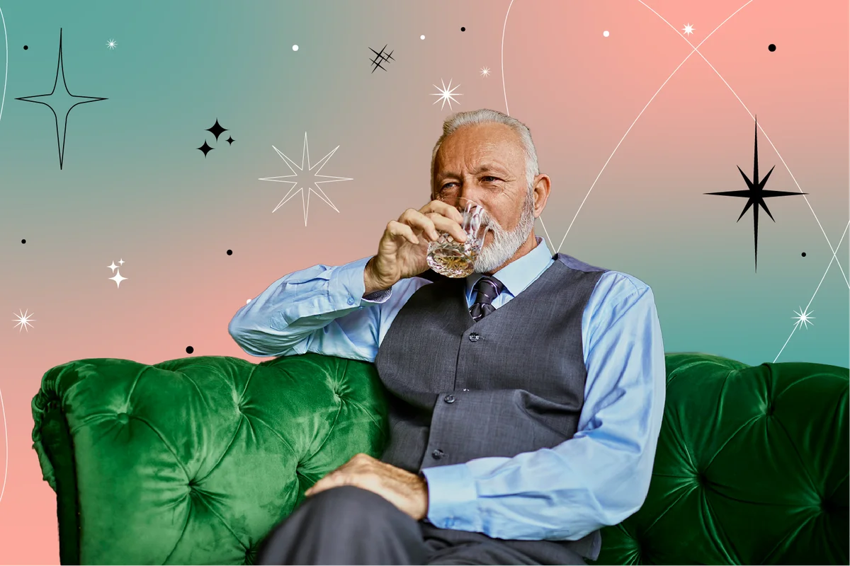 elegant senior man sitting on couch in a bar drinking from tumbler