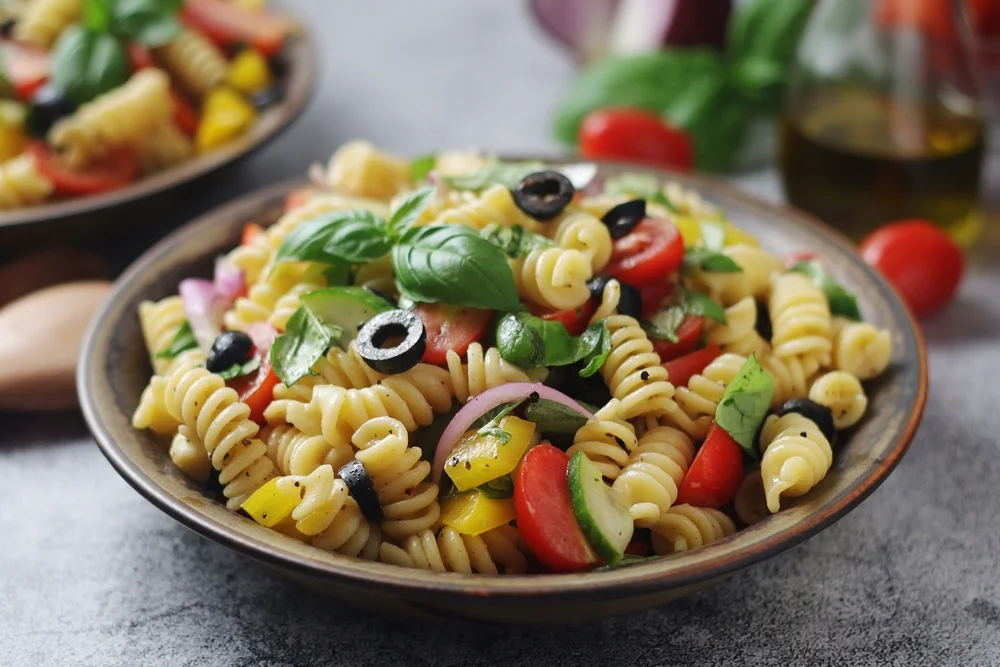 Closeup of a bowl of pasta salad with olives and tomatoes