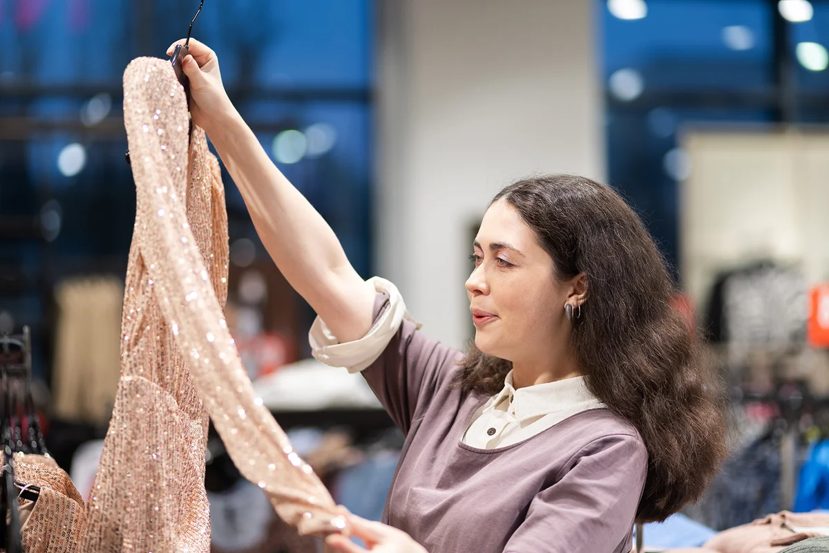 woman holds hanger with sparkly dress