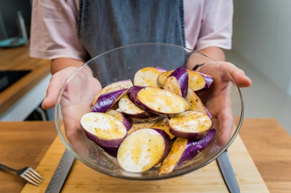 man's hands holding a bowl of sliced eggplant