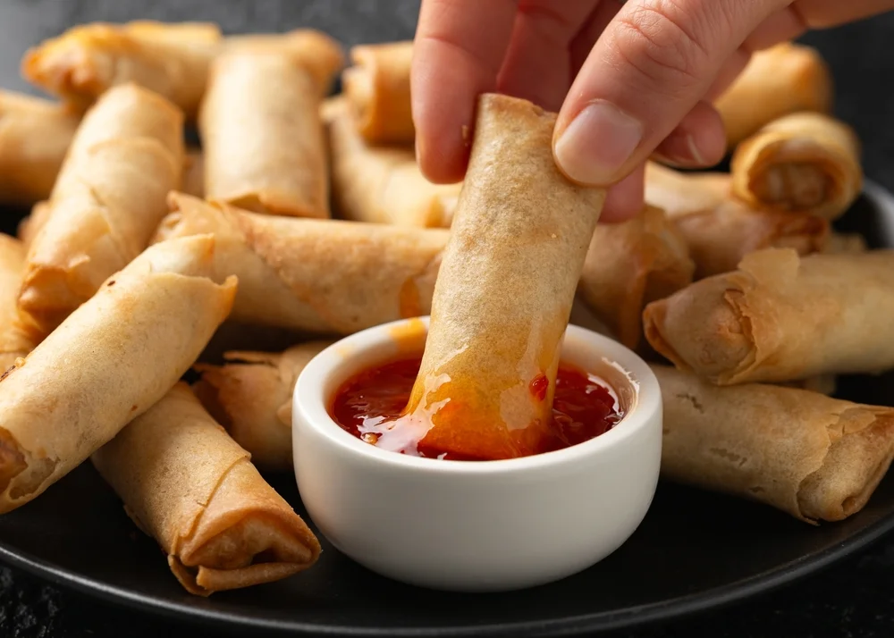 someone dipping spring rolls into duck sauce