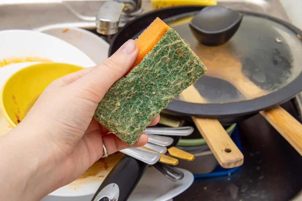 hand holding a gross sponge over a sink of dirty dishes