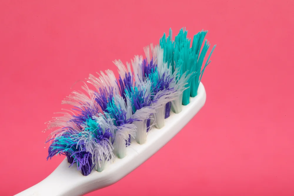 old, worn-out toothbrush on a hot pink background