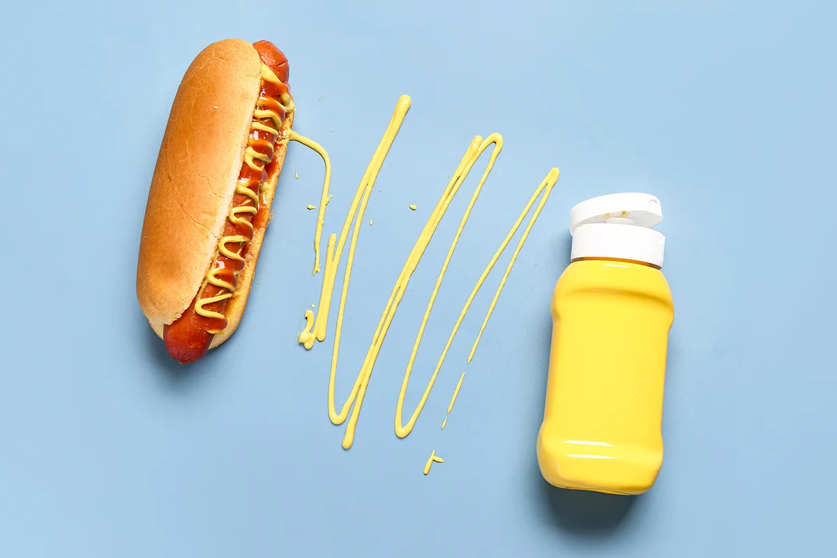 Tasty hot dog with bottle of mustard on blue background