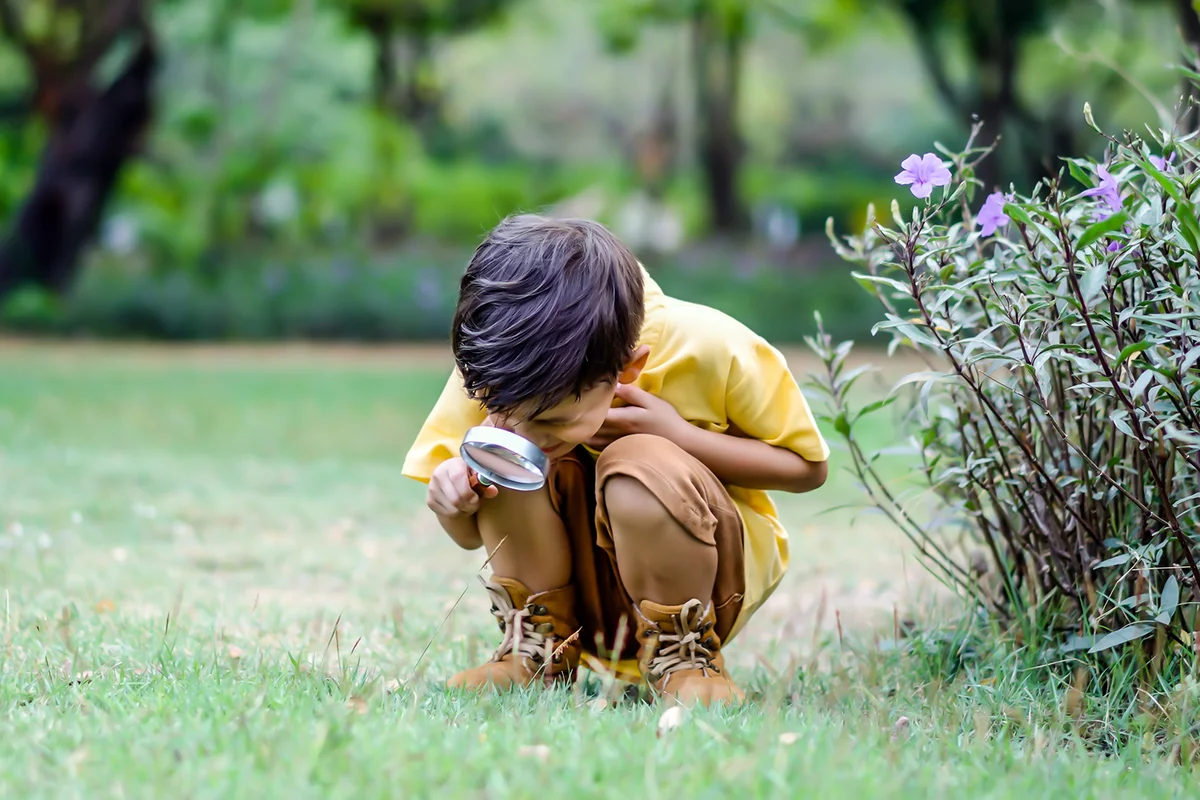 little boy exploring the nature with magnifying glass outdoors