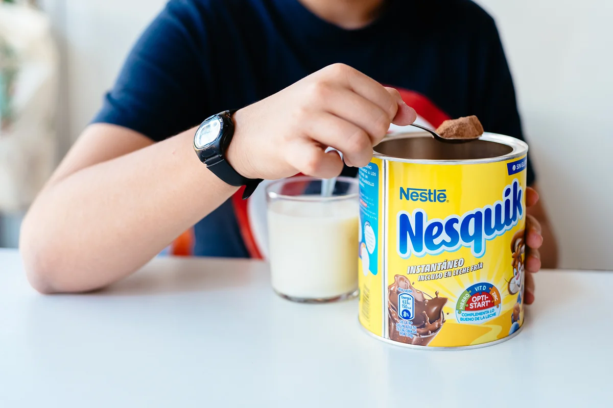 Boy serving Nesquik cocoa powder in a glass of milk