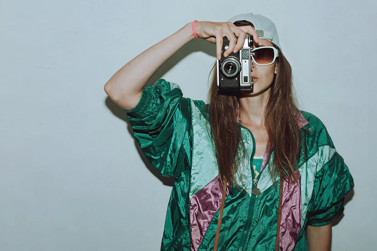 Fashionable girl in colorful trendy jacket and vintage retro sunglasses with camera film in 80s - 90s style.