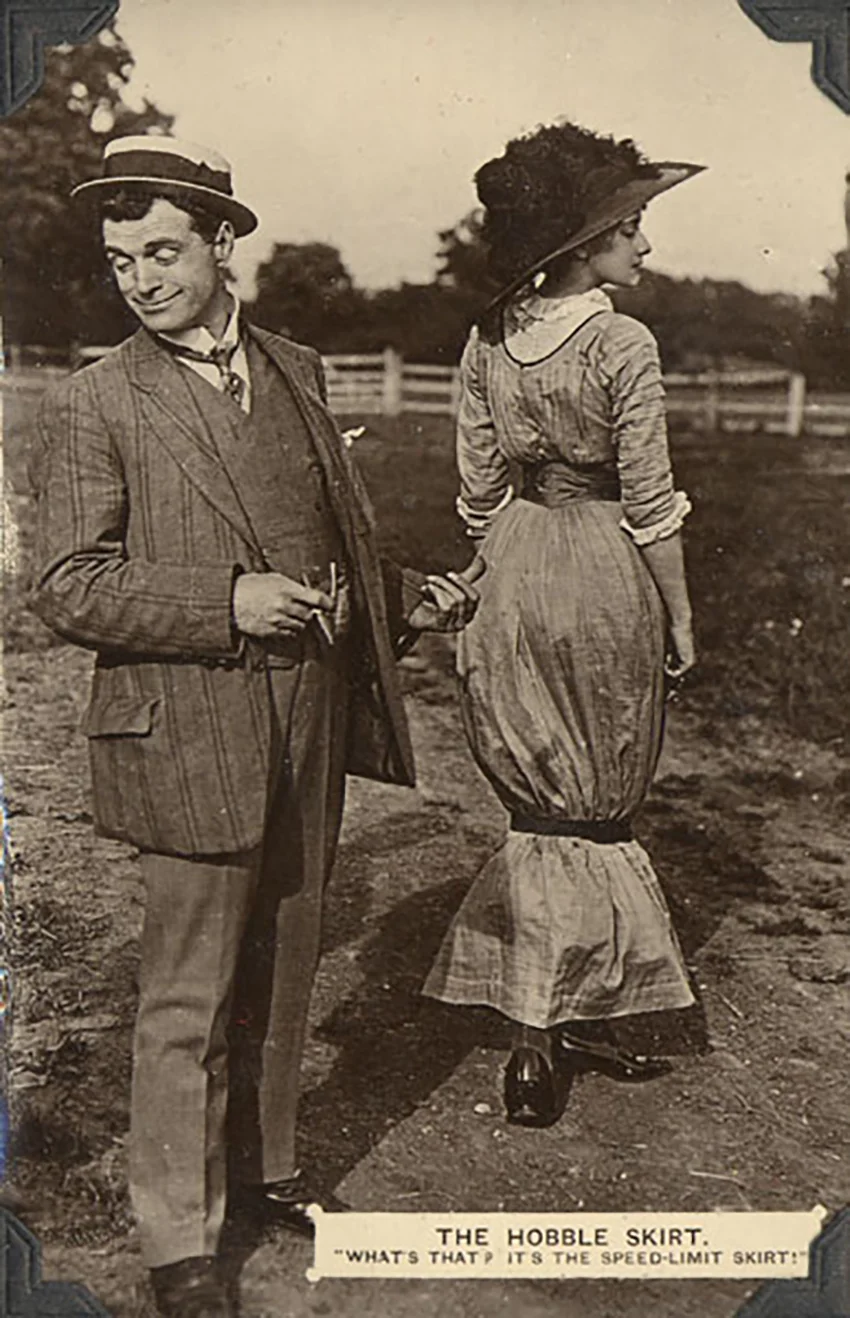 Woman wears a hobble skirt, man points to her with his thumb.