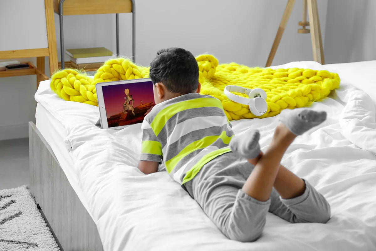Boy watching cartoons on tablet computer in bedroom