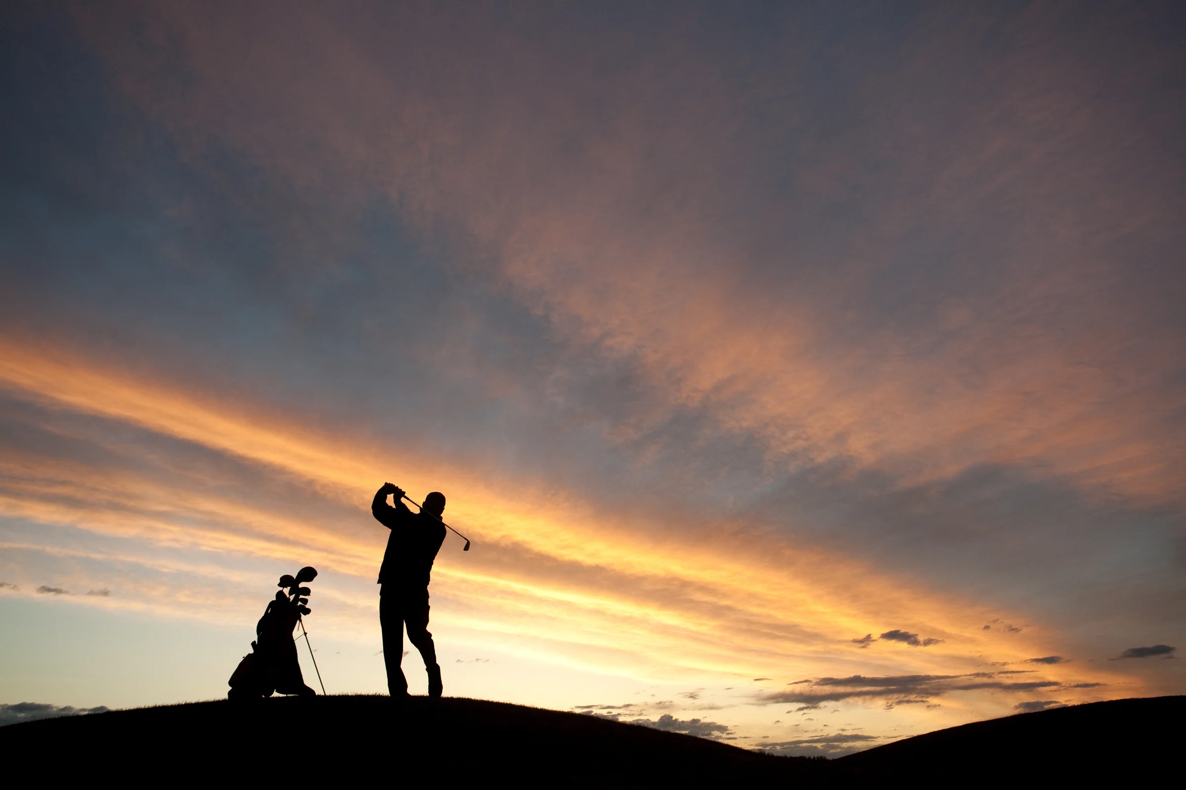 Golfer hitting a ball on a hill with the ball below his feet