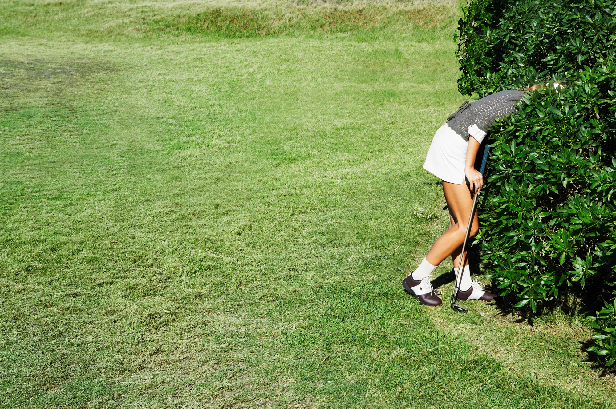 Woman looks for golf ball in the bushes